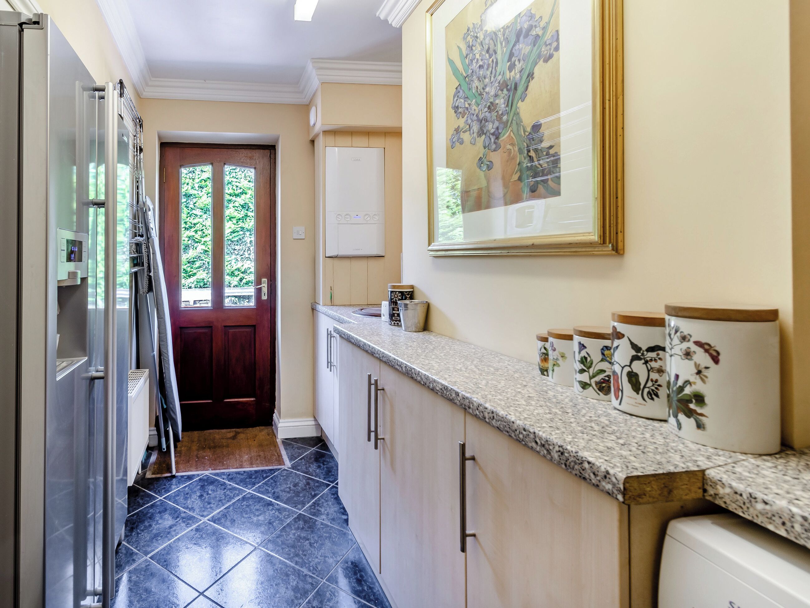 A kitchen with a dark tile floor, a wooden door, a white refrigerator, and a countertop with decorative jars.