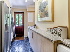 A kitchen with a dark tile floor, a wooden door, a white refrigerator, and a countertop with decorative jars.