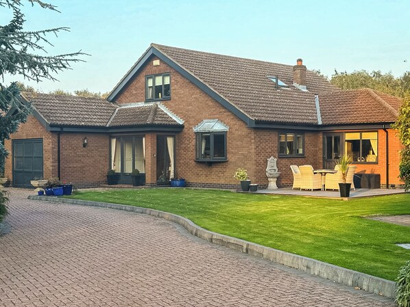 A two-story brick house with a tiled roof, a front porch with outdoor furniture, and a well-maintained lawn.
