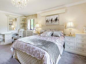 A bedroom with a large bed, a desk, a chair, and a chandelier.