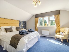 A hotel room with a large bed, a chair, a window with curtains, and a radiator.