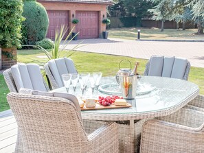 A round glass table with wicker chairs, a bottle of champagne, glasses, and a fruit platter.