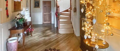 Un pasillo con suelo de madera, una escalera, una araña y una pared decorada con luces y adornos.