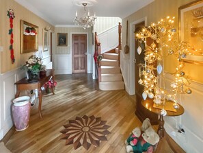 A hallway with a wooden floor, a staircase, a chandelier, and a wall decorated with lights and ornaments.