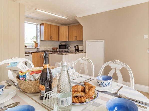 A breakfast setup with croissants, a bottle of wine, and a basket of snacks.