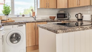 Eine moderne Küche mit Holzausstattung, einer integrierten Waschmaschine, einer Mikrowelle und einem Wasserkocher.