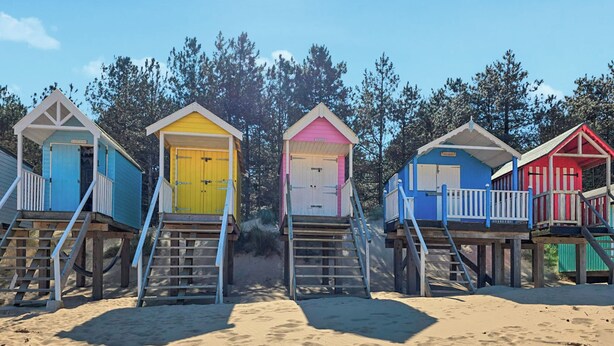 Eine Reihe von Strandkörben mit Treppen, vor einer Sandküste und Bäumen.