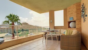 A balcony with a wicker sofa, a dining table, and a palm tree. - Apartment with mountain and sea views, parking (Cabo de Palos)