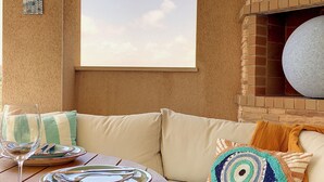 A cozy seating area with a round wooden table set for two, a wicker ottoman, and a cushioned bench with decorative pillows. - Apartment with mountain and sea views, parking (Cabo de Palos)
