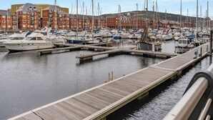 Un puerto deportivo con varias embarcaciones amarradas, muelles de madera y edificios de ladrillo rojo al fondo.