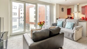 Una sala moderna con un sofá gris, una mesita con un florero, y un ventanal con vistas a la ciudad.