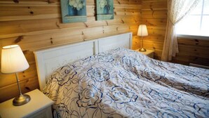 Dormitorio de cabaña de madera con una cama, dos lámparas de pared y dos cuadros florales.