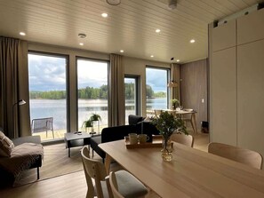 Una sala de estar moderna con una gran mesa de comedor, asientos cómodos y ventanas amplias con vistas a un lago.
