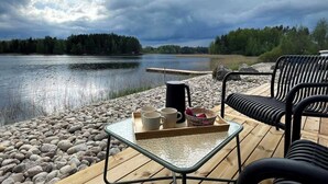 A lakeside deck with outdoor seating and a table set with mugs and a kettle.