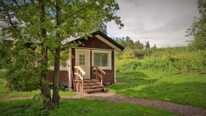 Een klein houten vakantiehuisje met een veranda en een raam, omringd door groen.