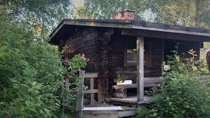 Een houten blokhut in rustieke stijl met een veranda, omgeven door weelderige begroeiing.