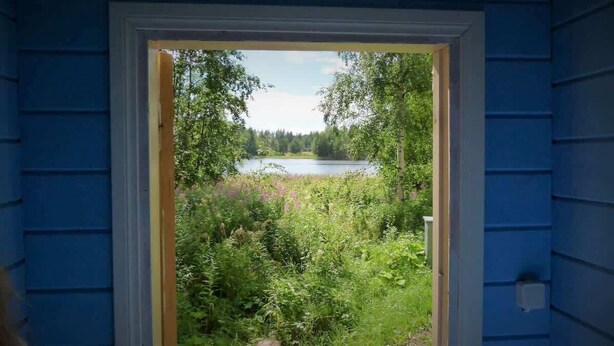 Uitzicht door een deuropening op een natuurlandschap met een meer en weelderige begroeiing.