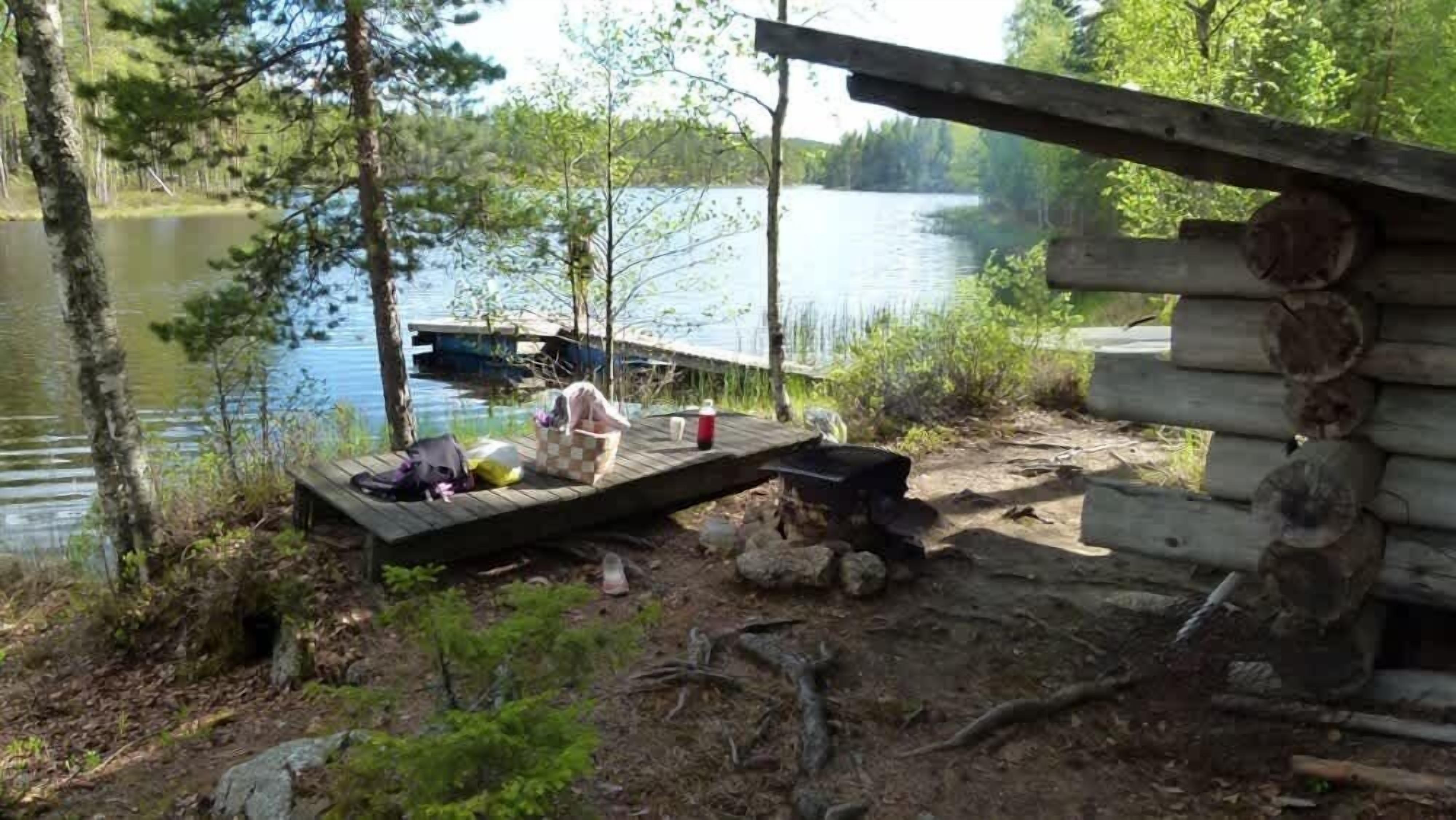 Un chalet rustique avec un quai s’avançant dans un lac, le tout entouré d’arbres.