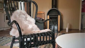 Una sala de estar acogedora con un perro blanco y esponjoso en una silla de metal negro, una mesa blanca, una chimenea y un reloj de pared.