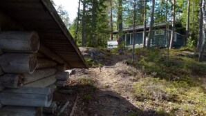 Una cabaña de troncos con un sendero de tierra que conduce a un edificio moderno en un área boscosa.
