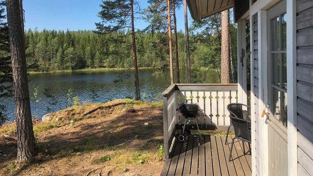 A wooden deck with a grill and chairs overlooking a lake, surrounded by trees.