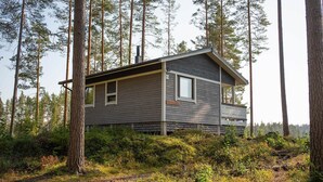 A cabin with a balcony, surrounded by tall trees and a forested area.