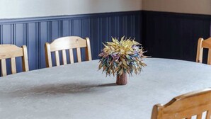 A dining area with a round table, wooden chairs, a woven pendant light, a wall clock, and a shelf with decorative items. - Enchanting cottage in the woods, by the lake (Orivesi)