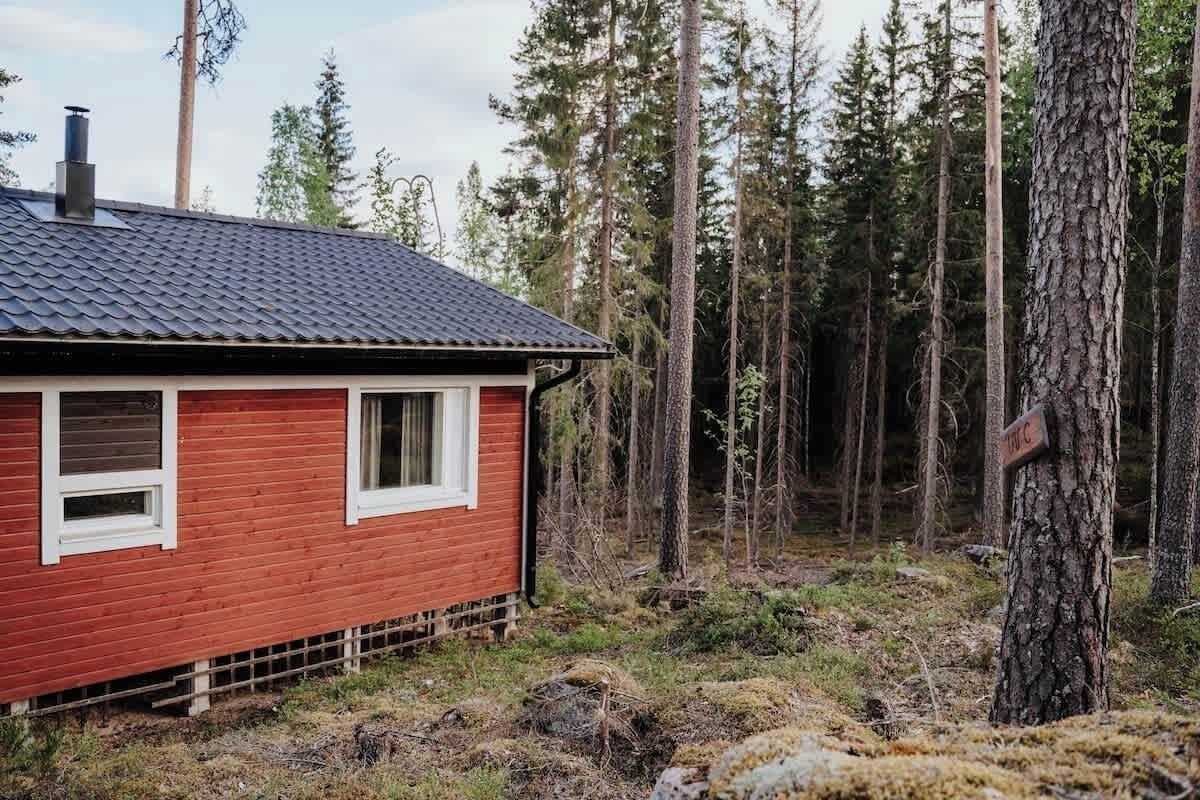 Een rode houten hut met een donker dak, omgeven door een bos.