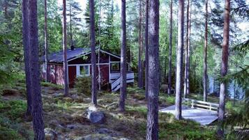 A cabin in a forest with a wooden deck and a small porch.