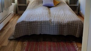A bedroom with a wooden ceiling, floral wallpaper, a bed with a patterned bedspread, two bedside lamps, and a red rug. - Silent, private cottage by lake,  sauna and boat (Orivesi)