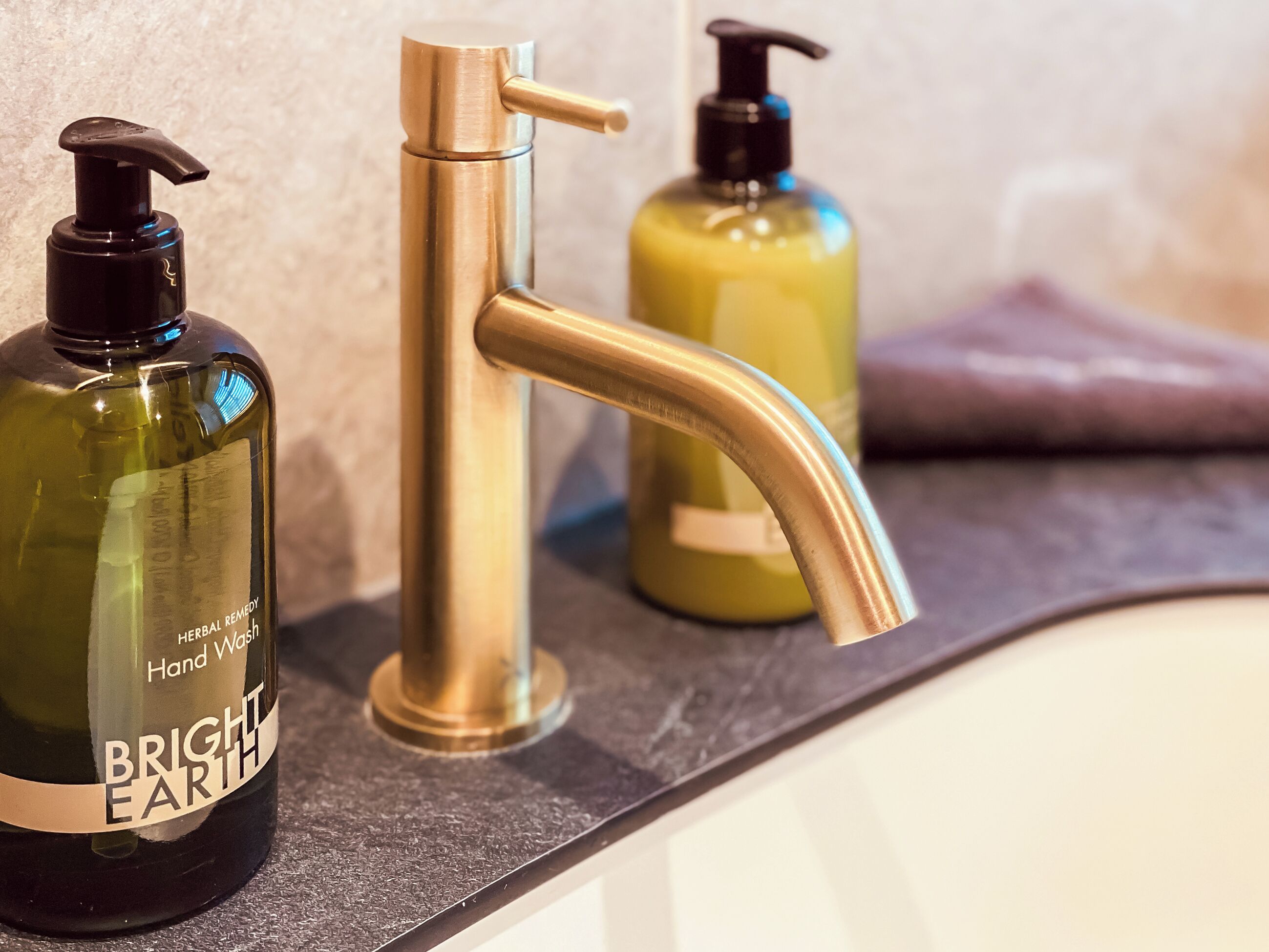 A bathroom counter with a gold faucet and two bottles of hand soap.