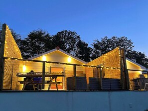 A two-story building with a sloped roof, wooden exterior, and string lights. - Dragonfly Cottage-UK39919 (Ballaugh)