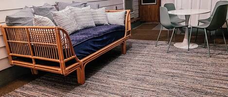 A room with a wicker sofa, a small round table with chairs, and a patterned rug.