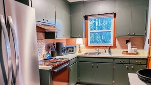 Een keuken met een roestvrijstalen koelkast, een magnetron, een fornuis en groene keukenkastjes.