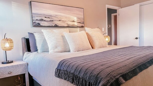 Een slaapkamer met een bed, nachtkastjes, een lamp en een schilderij aan de muur.