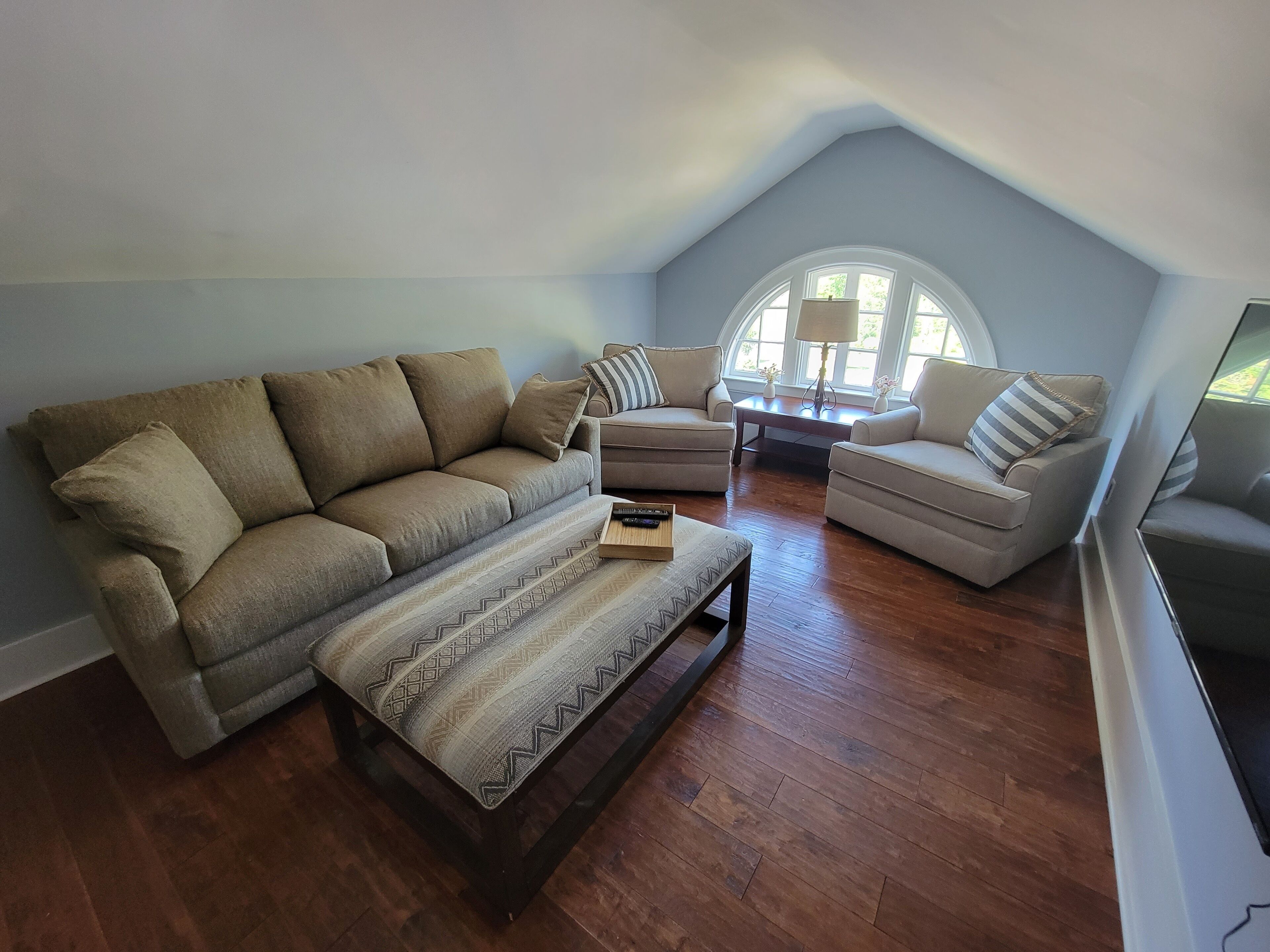A living room with a high ceiling, a large window, and a wooden floor.