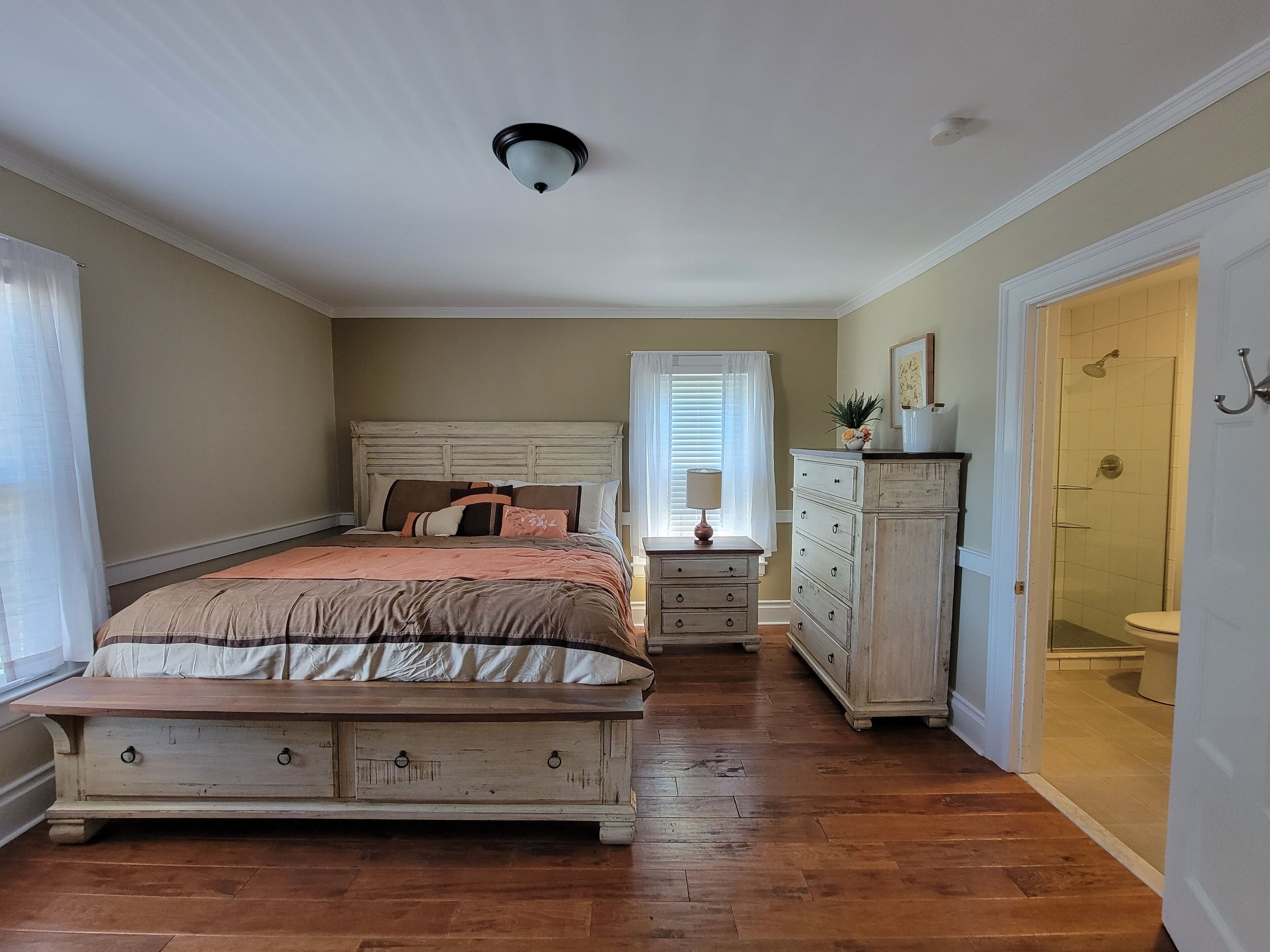 Un dormitorio con cama, cómoda, mesita de noche y una puerta que da al baño.