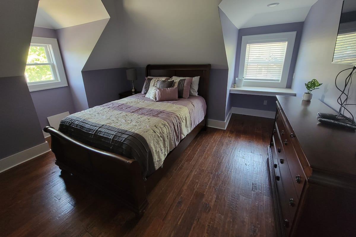 A bedroom with a bed, wooden dresser, and a window with blinds.