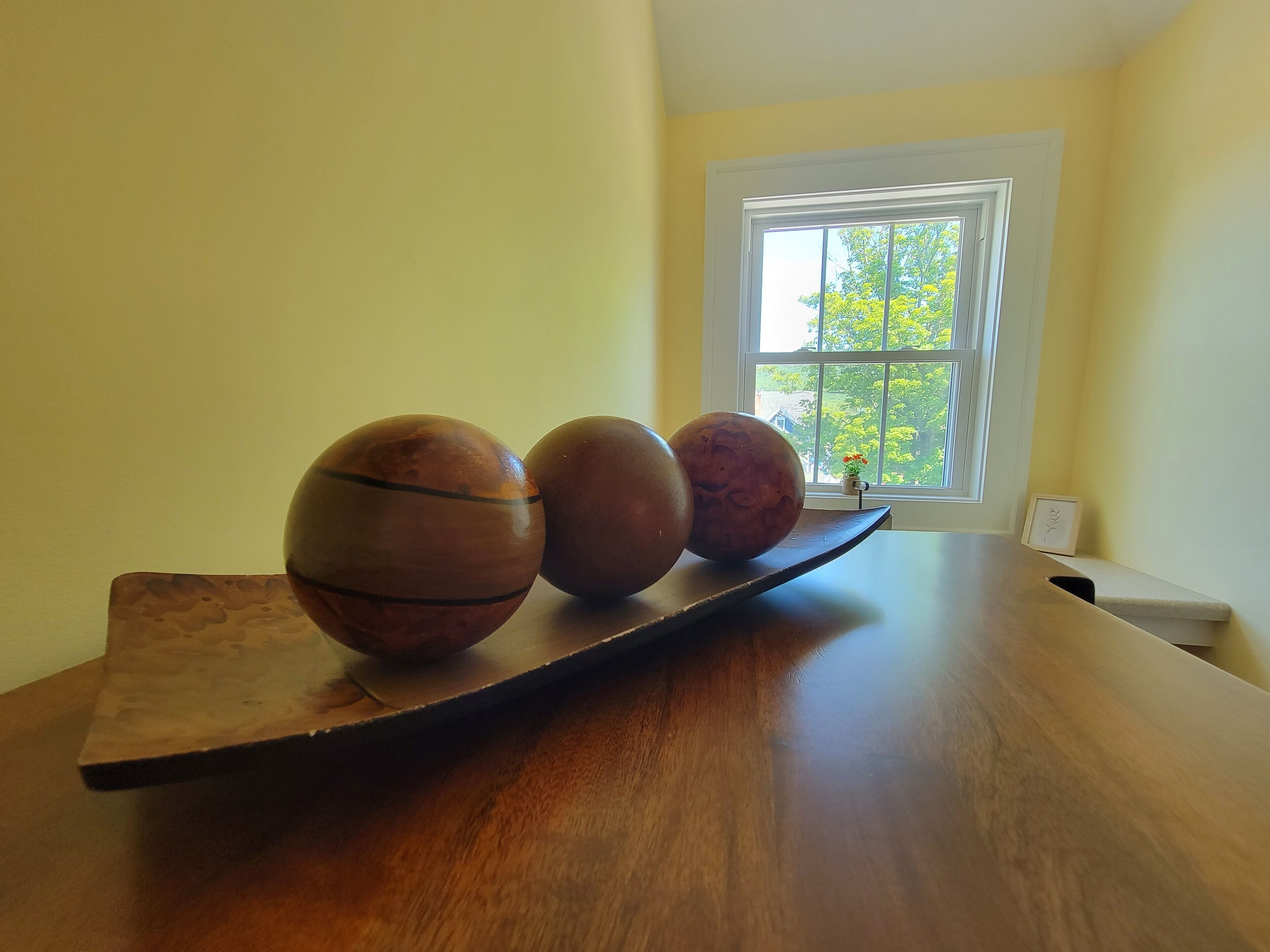 A wooden table with three spherical objects and a window with a view of trees and a building.