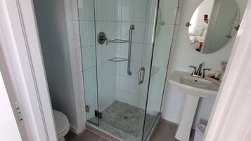 A bathroom with a glass-enclosed shower, a toilet, and a sink with a mirror.