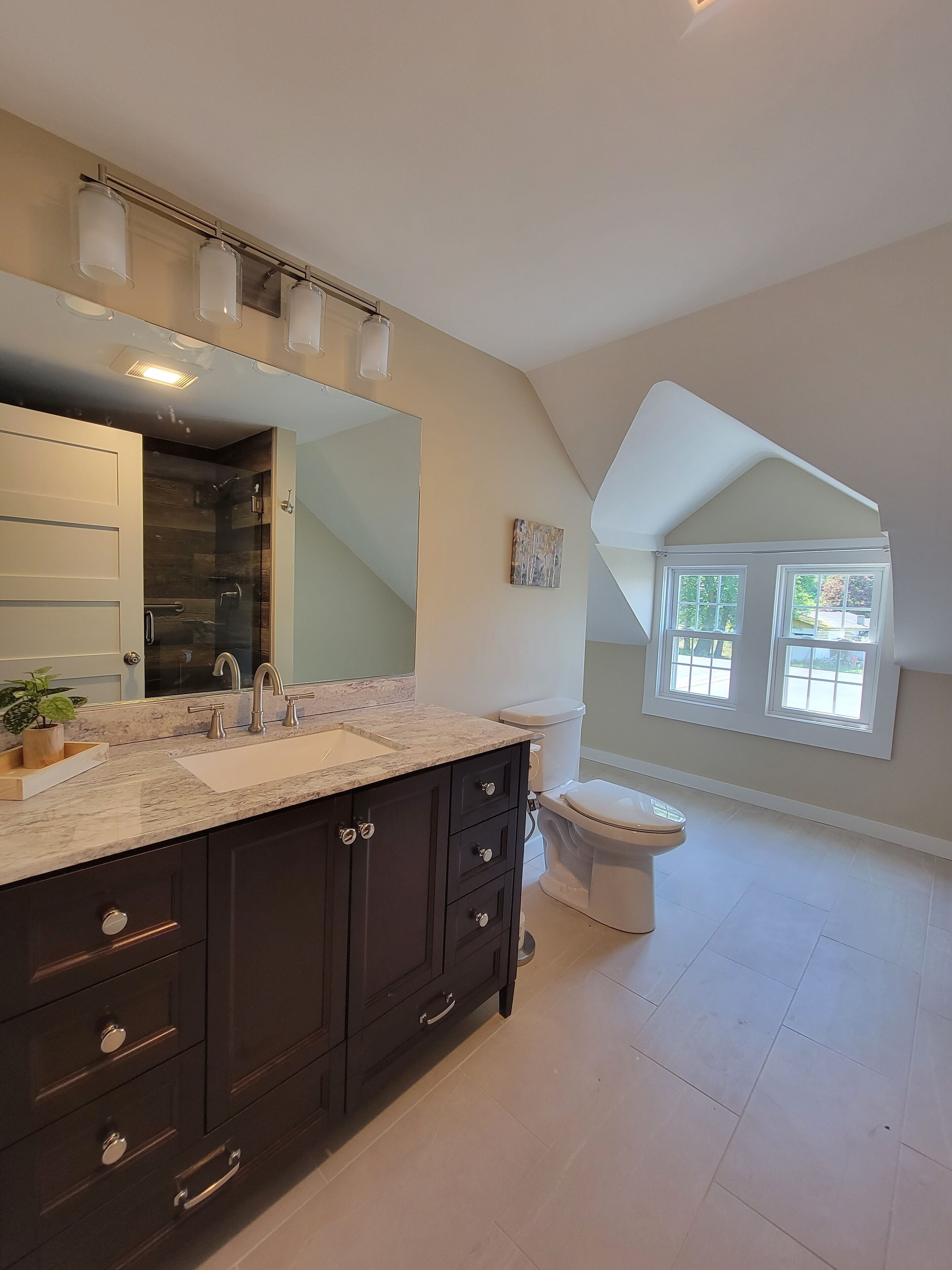 Un baño moderno con un espejo grande, muebles oscuros y un inodoro blanco.