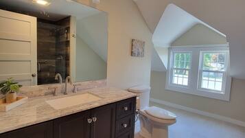 Un baño moderno con un espejo grande, muebles oscuros y un inodoro blanco.