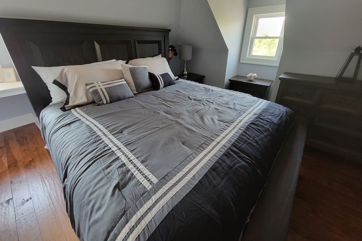 A bedroom with a large bed, dark wooden headboard, and a window with a view of greenery.