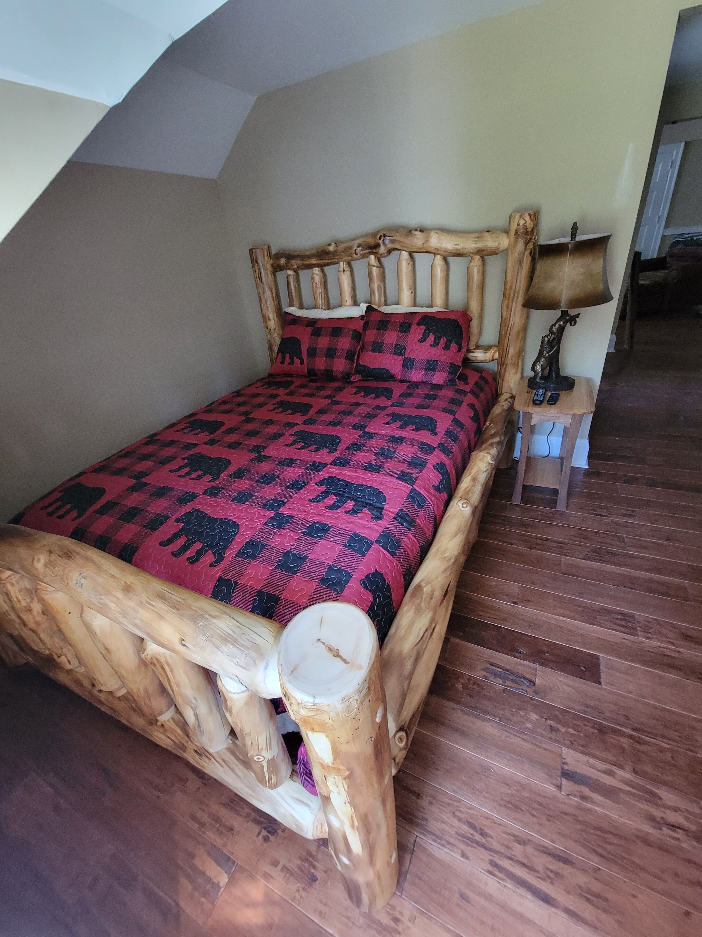 A bed with a wooden headboard and a red and black checkered bedspread.