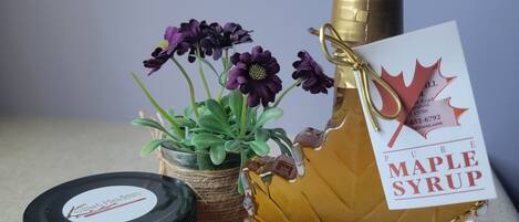 A bottle of maple syrup, a jar of jam, a thank you card, and a small potted plant.