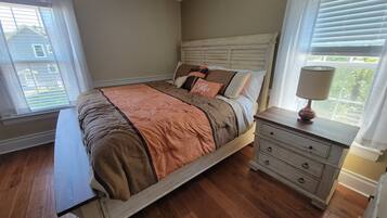 A bedroom with a wooden bed, a nightstand with a lamp, and a window with blinds.