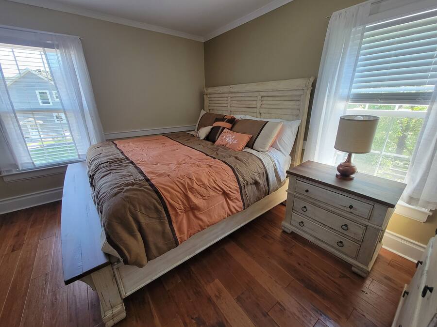 A bedroom with a wooden bed, a nightstand with a lamp, and a window with blinds.