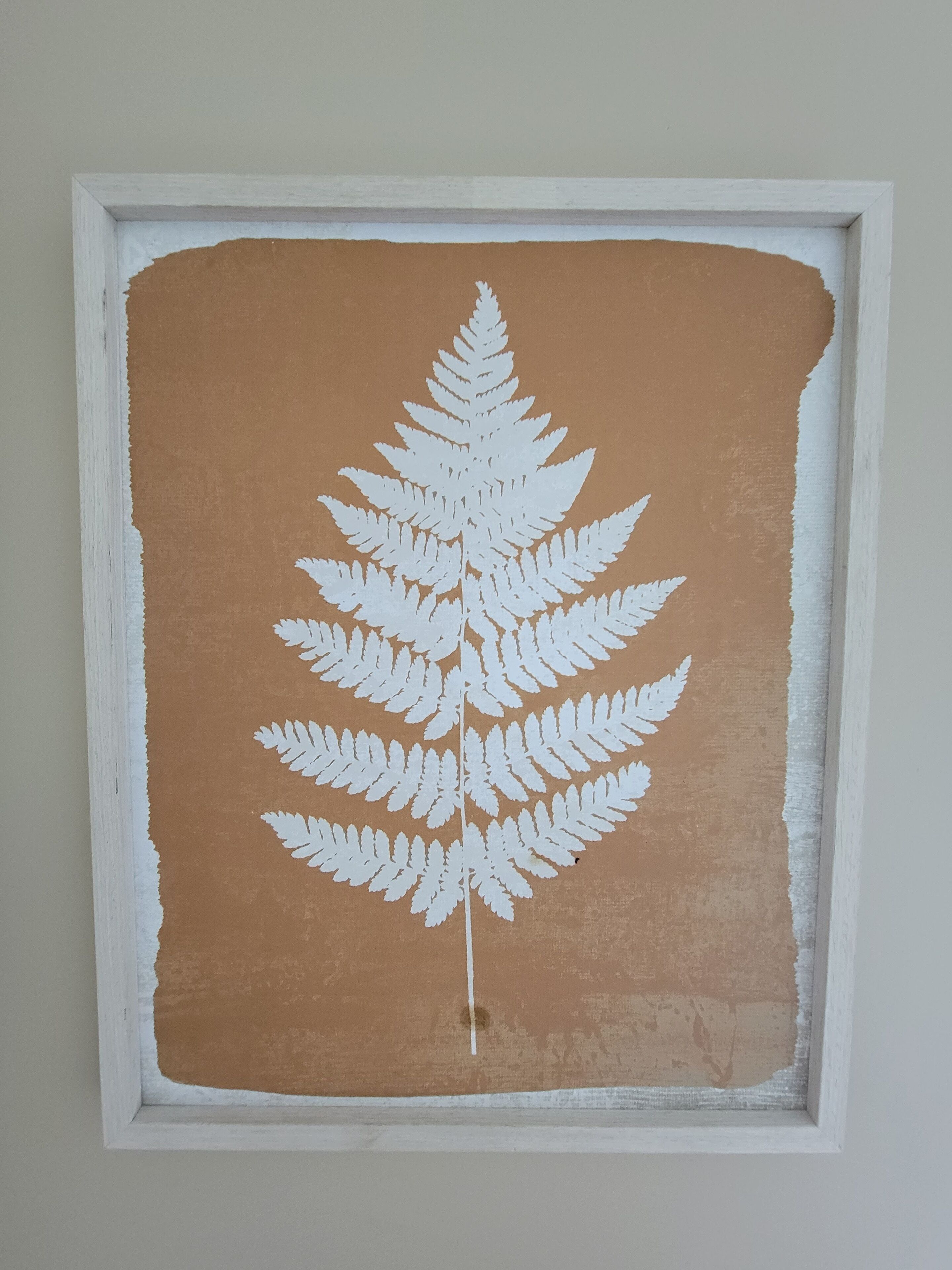 Une œuvre d’art encadrée représentant une fougère sur un fond brun texturé.