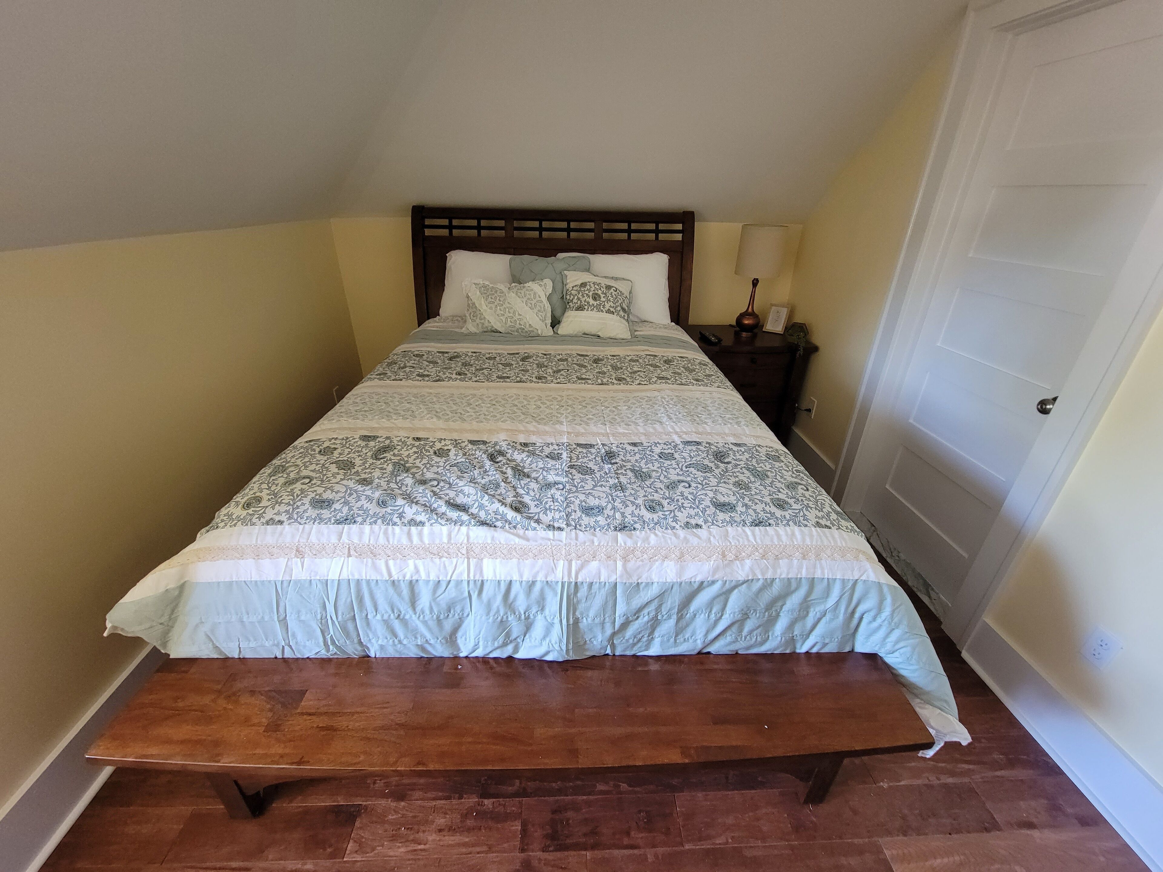 A single bed with a wooden headboard, a bedside table with a lamp, and a door to the right.