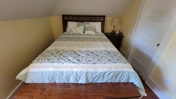 A single bed with a wooden headboard, a bedside table with a lamp, and a door to the right.